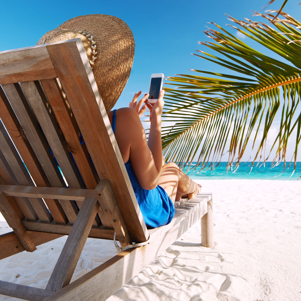 Digital detox - Une femme sur une plage paradisiaque assise sur un transat et qui utilise son smartphone