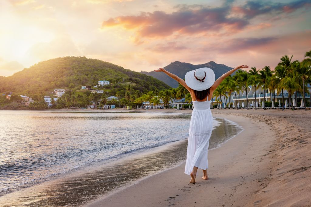 Woman walking on beach in Antigua with her arms raised