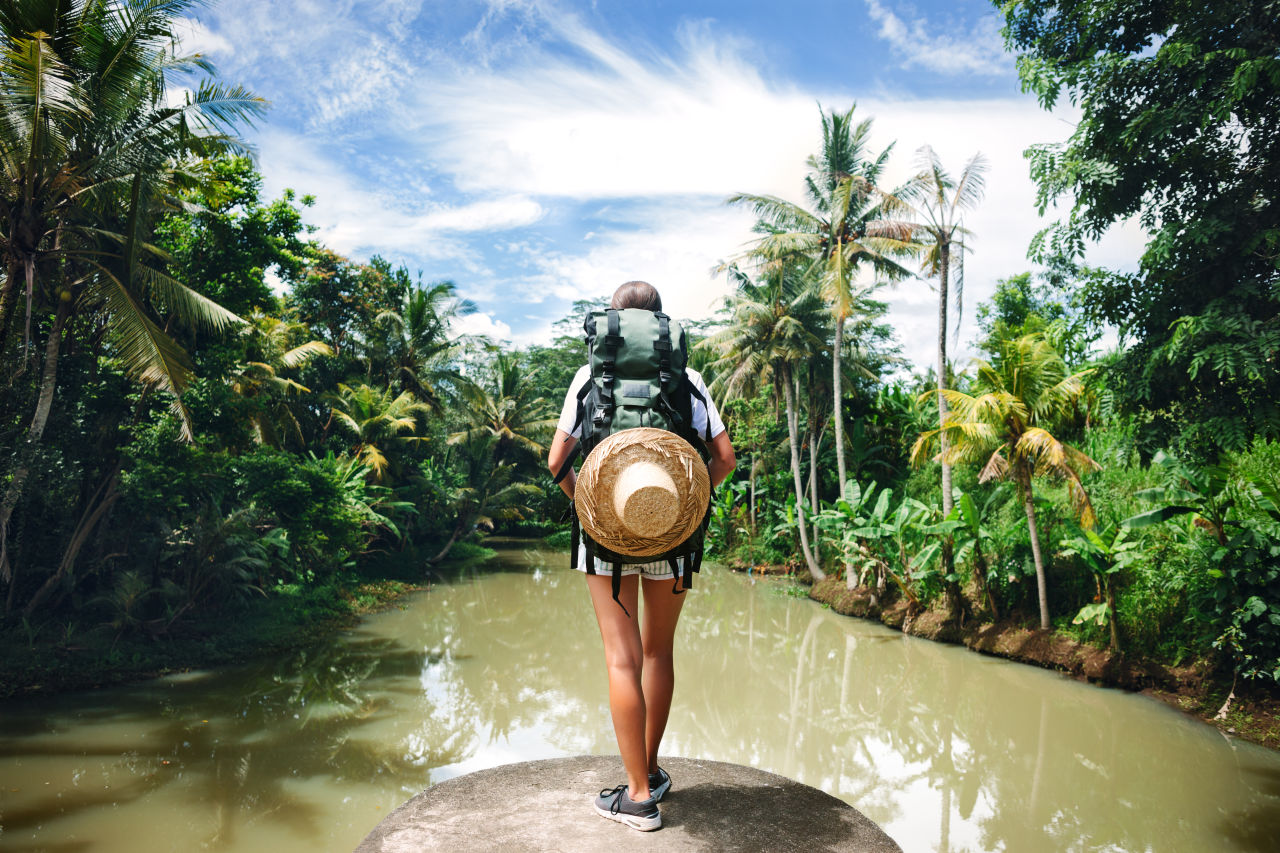 Femme avec sac à dos debout près d'une rivière tropicale