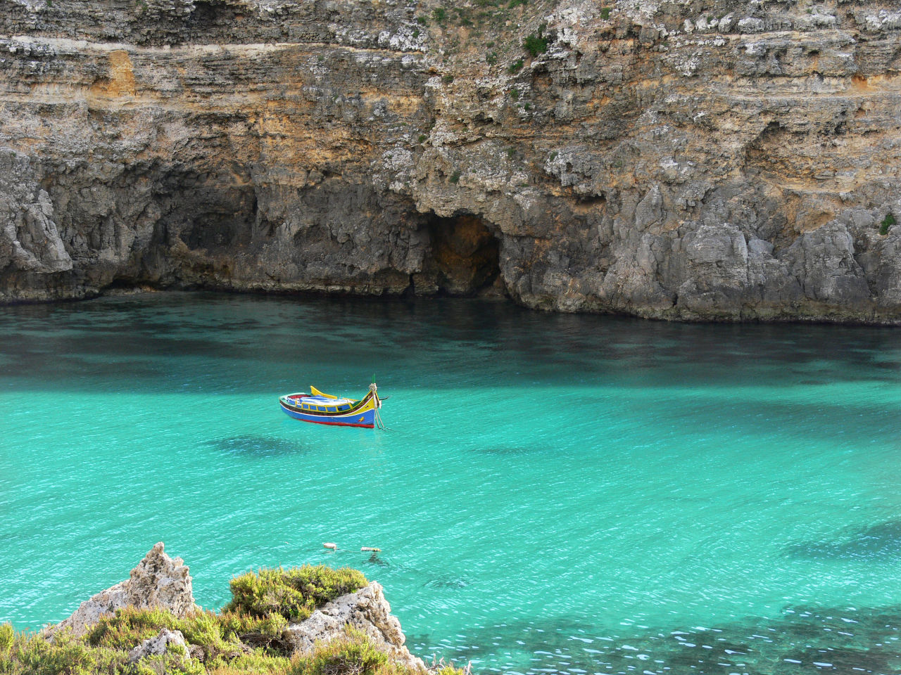 Buntes Fischerboot, das im kristallklaren türkisfarbenen Wasser in einer Bucht der Insel Gozo schwimmt