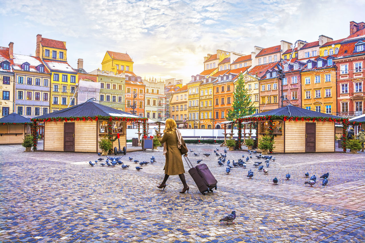 Traveler young woman walking with luggage on the Old Town Square with the Christmas market in Warsaw in the winter, Poland.