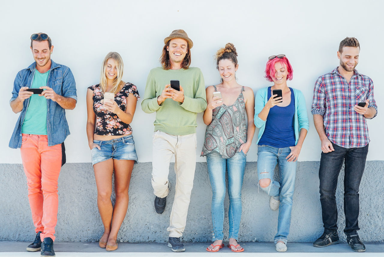 People standing against a wall on their phones