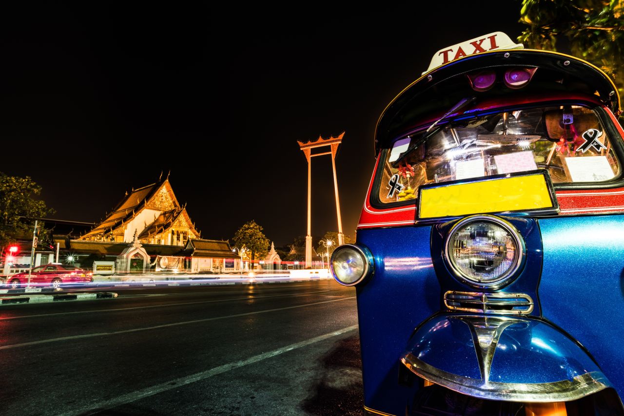 Eine Autorikscha – auch Tuk-Tuk genannt – vor der erleuchteten Nachtkulisse von Bangkok