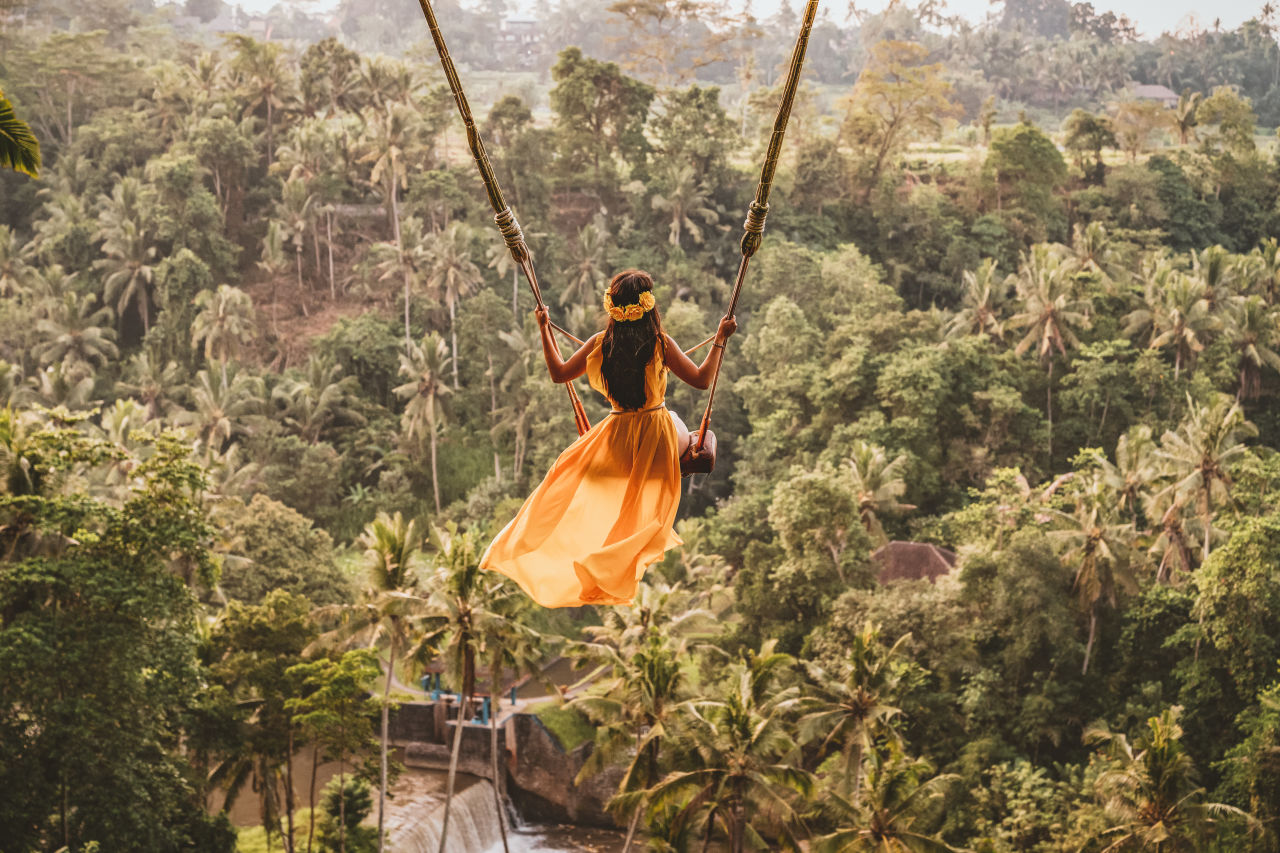 Vrouw in gele jurk op hoge schommel tussen de palmbomen op Bali