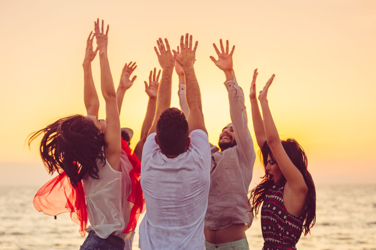 Een gelukkige groep mensen op het strand met hun handen omhoog.