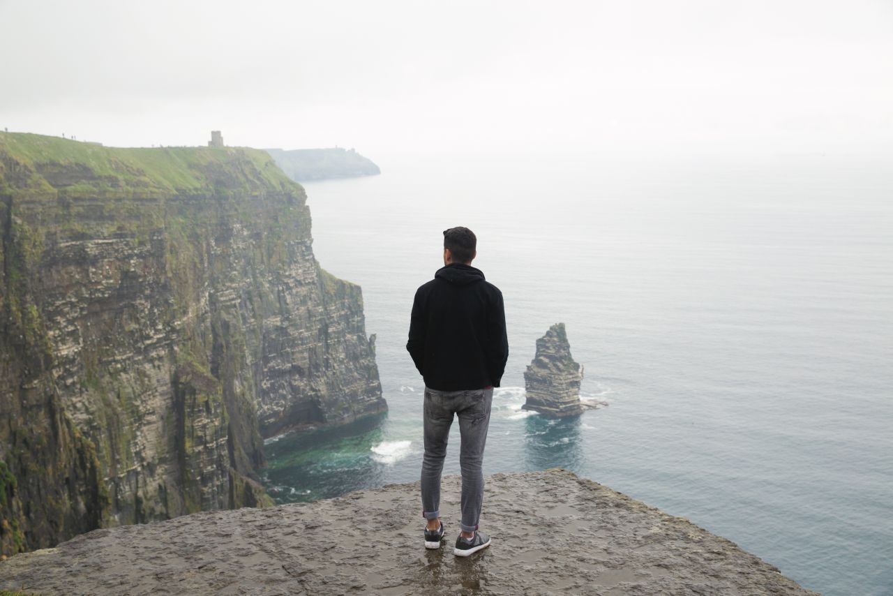 A guy looking out at the cliffs of Moher with his back turned