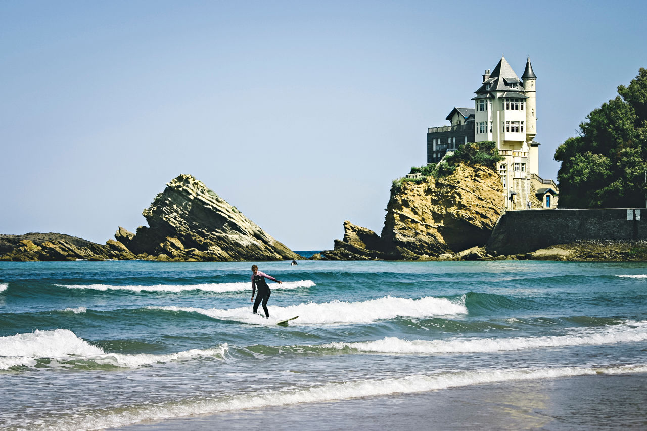 Vagues de Biarritz avec un surfeur, des rocher et la villa Belza au second plan