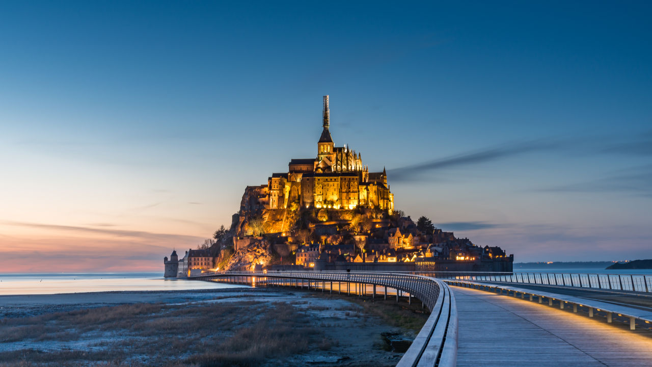 A medieval abbey perched on a rocky island in a bay, surrounded by water at low tide