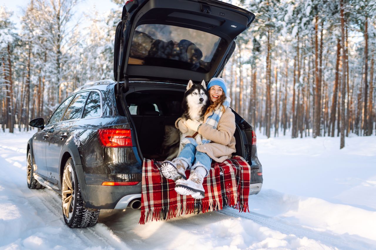  5 Holiday Pet Travel Mistakes  - Woman sits with her dog in the snow inside the back of her car