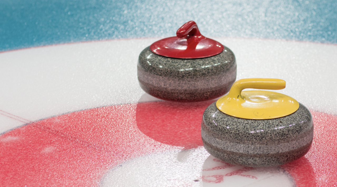 Red and yellow curling stones positioned inside the house target during competition