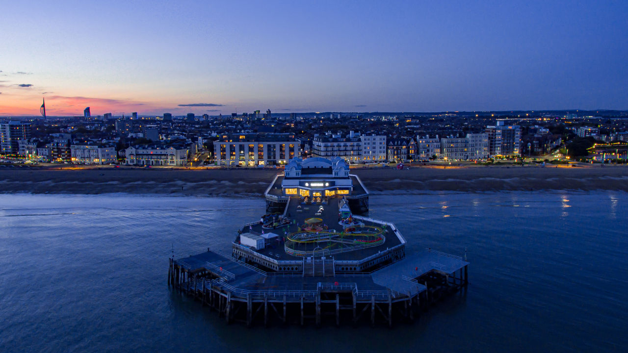 Aerial drone view of South Parade Pier in Southsea, Portsmouth, England, lit up at dusk with the city skyline visible in the background, one of the filming locations for Project Hail Mary.