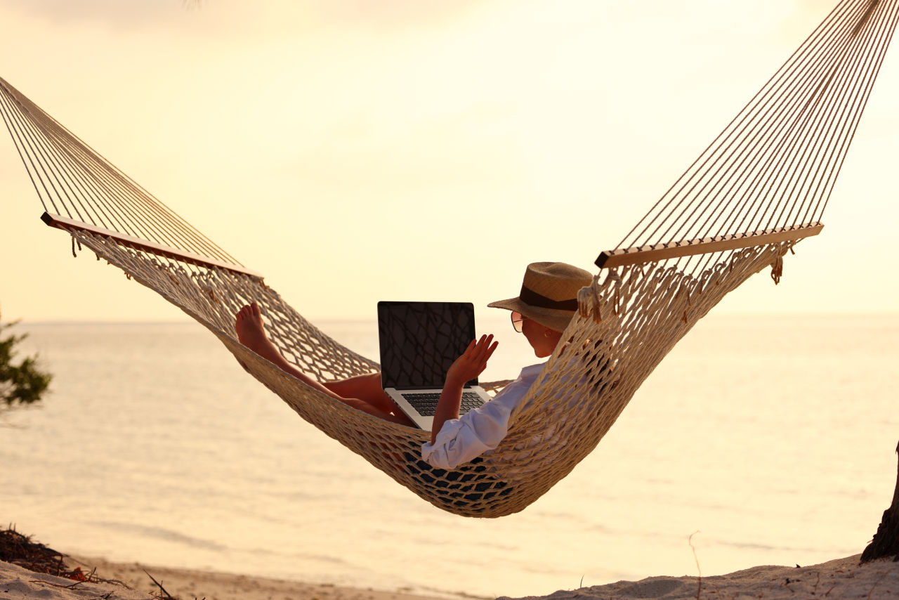 Digital nomad working on laptop in hammock by the beach in Costa Rica at sunset