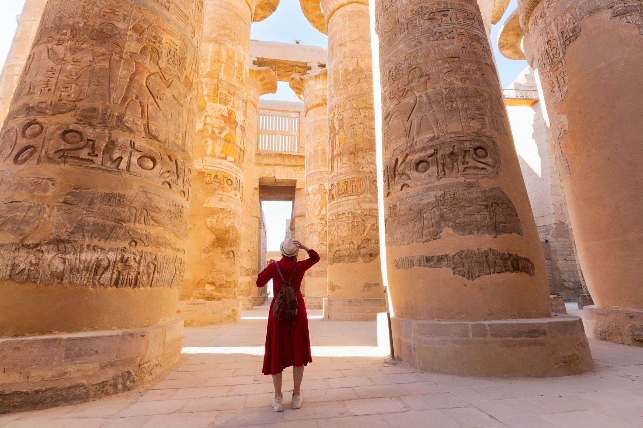 * Tourist exploring towering ancient Egyptian columns covered in hieroglyphics at Luxor Temple.
