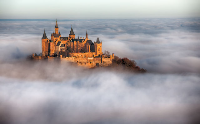 Hohenzollern castle sitting on top of a mountain with clouds surrounding it