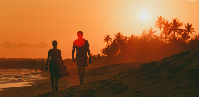 couple marchant main dans la main sur une plage au coucher du soleil pendant un voyage de noces pas cher