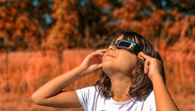Meisje draagt een zonsverduisteringbril tijdens de zonsverduistering. | Girl wearing eclipse sunglasses during solar eclipse.