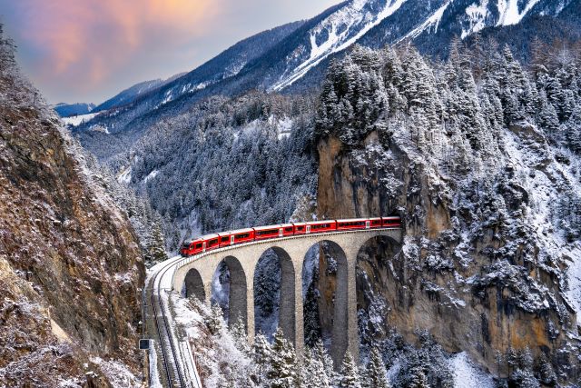 Trein die over een burg rijdt in een winters berglandschap.