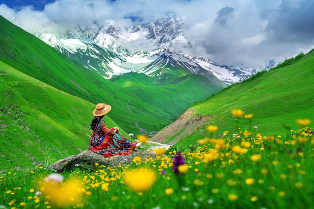 Tourist sitting on the rock at green pasture against highest georgian mountain Shkhara near Ushguli in Georgia.