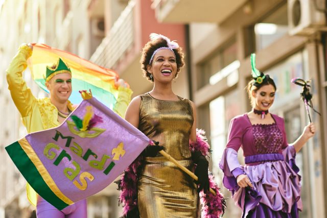 Mardi Gras parade performers holding a Mardi Gras flag and rainbow flag during celebration in New Orleans
