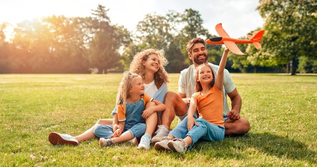 Parents and children sitting together in a sunny park with a toy airplane, reflecting outdoor family life and community safety