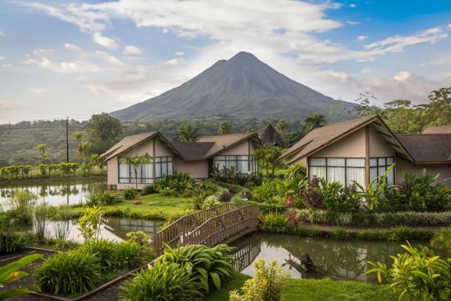 Luxury villas surrounded by tropical gardens with Arenal Volcano towering in the background at Montaña de Fuego Resort in Costa Rica.