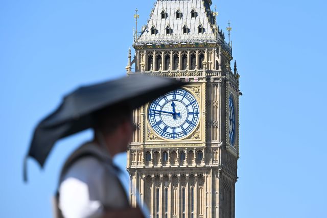 Big Ben in London during a summer heatwave with a pedestrian using an umbrella for shade