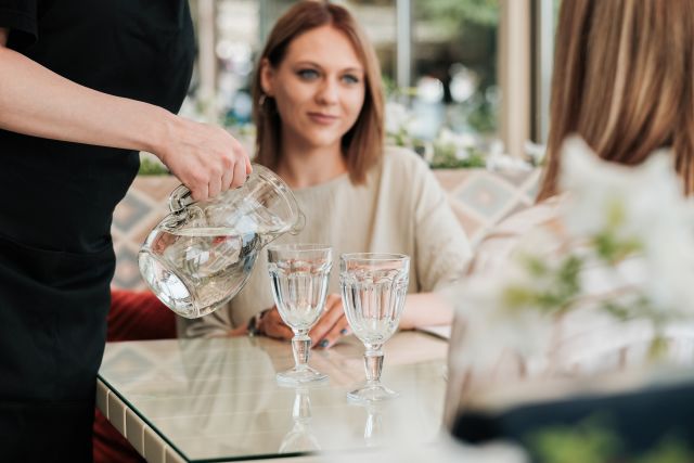 Waiter pouring water for guests at a restaurant table during a meal