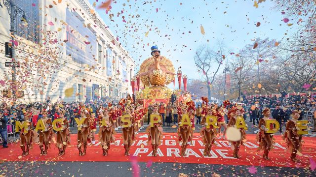 Tom Turkey float and dancers holding Macy's Parade letters under falling confetti on Central Park West