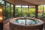 Private indoor hot tub surrounded by floor-to-ceiling windows overlooking lush tropical gardens.